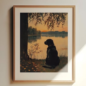 Pode incluir: Um labrador retriever preto está sentado à beira de um lago ao pôr do sol, olhando para a água. O cão está silhutado contra o céu laranja e as árvores no fundo.