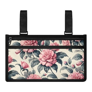 Może przedstawiać: Czarny i kremowy organizer z kwiatowym wzorem różowych róż i szarych liści. Organizer ma czarny zamek błyskawiczny i dwa czarne paski na górze. Kwiatowy wzór powtarza się na przodzie.