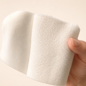 May include: A white rectangular cloth with two distinct textures. One side features a smooth, flat surface, while the other side has a soft, looped terry fabric texture. The cloth is folded over to display both sides of the white material clearly.