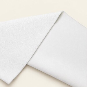 May include: A folded piece of white fabric showing two distinct textures. The top layer features a pebbled, granular surface, while the bottom layer displays a smooth, flat, and uniform weave. The material is bright white throughout the entire piece.