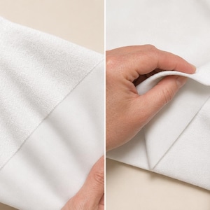 May include: A white fabric with two distinct textures, featuring a smooth, matte side and a contrasting soft, fuzzy, fleece-like side. The material is shown folded to display the difference between the two surfaces, highlighting the textile's dual-sided construction and clean, bright white color.