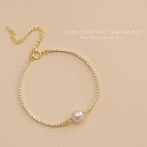 Könnte beinhalten: Goldenes Armband mit einer einzelnen Perle und kleinen, funkelnden Akzenten. Das Armband ist etwa 15 cm lang, mit einer 5 cm Verlängerungskette. Die Perle misst ca. 7 mm. Neutraler Hintergrund.