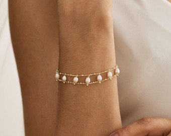 May include: A delicate gold chain bracelet featuring a double-layered design with small, evenly spaced white freshwater pearls suspended along the length of the chain. The bracelet has a polished metallic finish and a secure clasp mechanism.