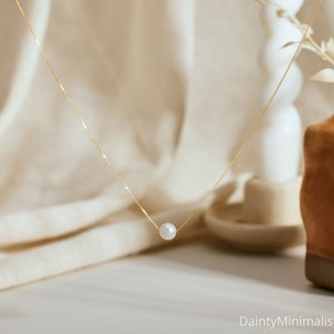 Puede incluir: Un delicado collar de cadena dorada con un solo colgante de perla blanca.