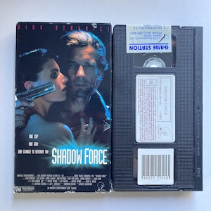 May include: A VHS tape of the movie "Shadow Force" featuring Dirk Benedict. The cover art shows a man and woman with a gun. The tape is black with white text and a barcode.