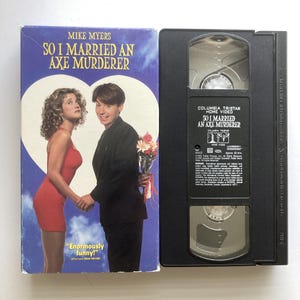 May include: A VHS tape and its cardboard sleeve for the film So I Married an Axe Murderer starring Mike Myers. The sleeve features a couple against a heart-shaped background, while the black plastic tape displays Columbia Tristar Home Video text.