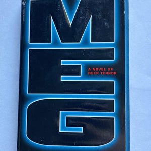 May include: A paperback book titled "MEG" with a black cover and blue neon lettering. The text "IF YOU SEE HER GLOW...IT'S TOO LATE" is at the top. The author's name, Steve Alten, is at the bottom.