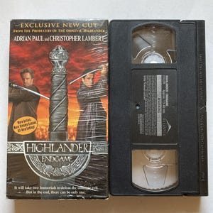 May include: A VHS tape and its cover for the movie "Highlander: Endgame." The cover features Adrian Paul and Christopher Lambert with swords, and the text "EXCLUSIVE NEW CUT." The tape is black.