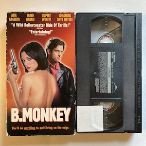 May include: A VHS tape and its cover for the movie "B. Monkey." The cover features a woman holding a gun and a man in a leather jacket. The title is in large, bold letters. The tape is black.