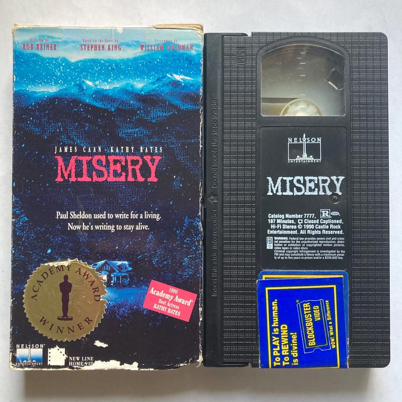 May include: A VHS tape and its case for the film "Misery". The case has a blue and white design with the title in red. The black tape has the title printed on it, along with a Blockbuster Video sticker.