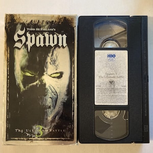 May include: A VHS tape and its case for "Spawn 3: The Ultimate Battle." The case features a dark, stylized image of Spawn's face with the title in bold white letters. The VHS tape is black with a white label.