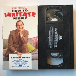 May include: VHS video cassette tape of the comedy classic "How to Irritate People" starring John Cleese. The cover features a photo of John Cleese sitting on a sofa with a yellow cushion. The text "A Comedy Classic" is printed below the photo.