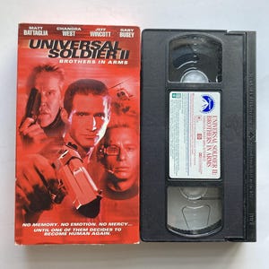 May include: A VHS tape of Universal Soldier II: Brothers in Arms with a red cover featuring actors Matt Battaglia, Chandra West, Jeff Wincott, and Gary Busey. The cover shows a helicopter and a handgun, with the text No memory. No emotion. No mercy.