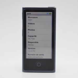 Peut inclure: Un iPod Nano gris foncé avec un écran affichant des informations. L'écran indique "Morceaux 1051", "Vidéos 0", "Photos 0", "Capacité 14.7 Go" et "Disponible 9.8 Go". L'appareil a un bouton circulaire en dessous.