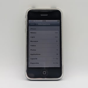 May include: A silver and black iPhone with the screen displaying information in French. The screen shows details like "Morceaux" (81), "Vidéos" (1), and "Applications" (28). The phone is on a white background.