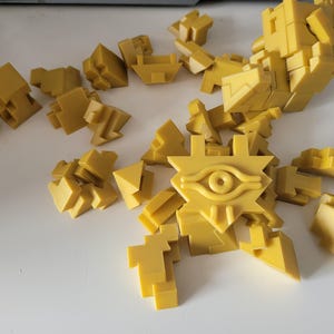 Op de afbeelding: Een gele 3D-puzzel van het oog van Horus, een symbool van bescherming en macht in de oude Egyptische mythologie. De puzzel bestaat uit veel kleine stukjes die in elkaar passen om het oog te vormen.