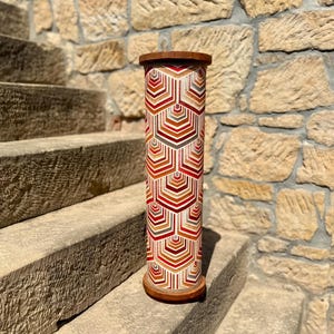 May include: A wooden cylinder with a geometric pattern in shades of red, orange, and white. The cylinder is standing on a set of stone steps.