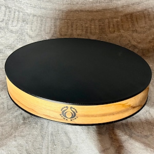 May include: A circular, black lid rests on a light-coloured wooden base. The base has a natural wood grain pattern. The text "SOMA BONA" is printed on the side of the base, along with a small graphic.