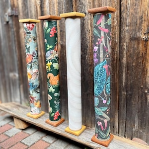 May include: Four cylindrical scratching posts with square wooden bases and tops. The first features a floral pattern, the second a green forest print with squirrels, the third a plain white textured surface, and the fourth a dark botanical print.