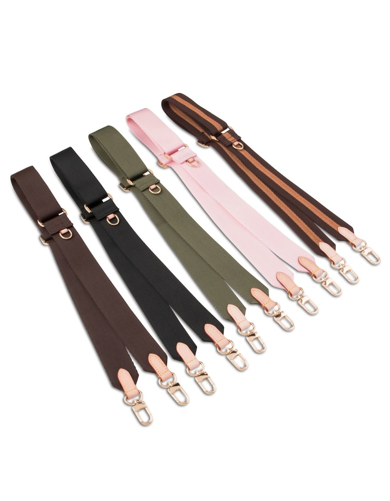 May include: Six different colored canvas straps with gold clasps and brown leather accents. The straps are arranged in a row, with the brown strap at the bottom and the striped strap at the top.