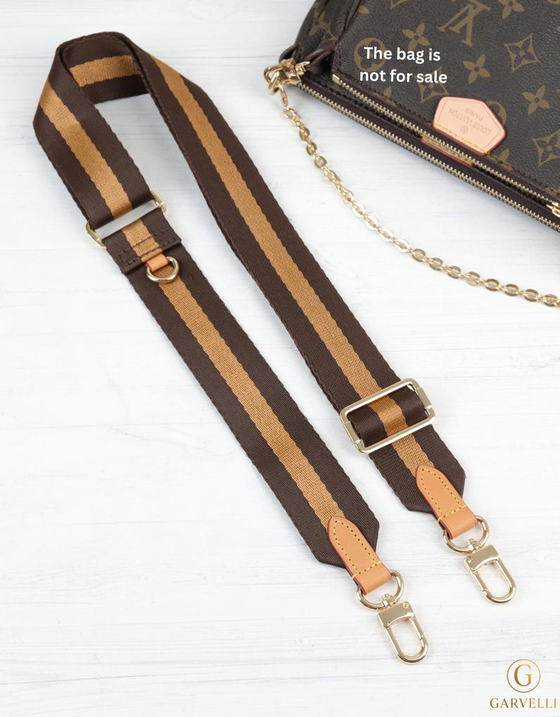 May include: Brown and tan striped handbag strap with gold-tone hardware. The strap features a brown base with a tan stripe down the center. The strap has gold-tone metal clasps and adjustable buckles. The bag is not for sale.