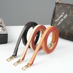 Puede incluir: Tres correas de cuero para bolso en negro, crema y rojo-naranja, cada una con cierres dorados. Las correas est&aacute;n enrolladas y expuestas sobre una superficie blanca. Un bolso marr&oacute;n con el texto "The bag is not for sale" est&aacute; en el fondo.