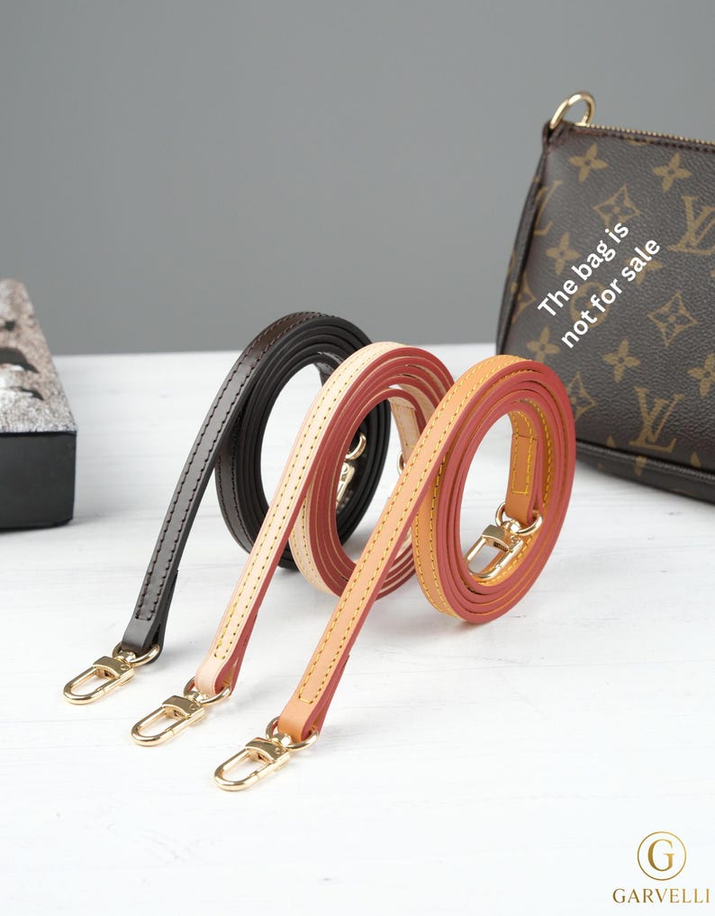 Puede incluir: Tres correas de cuero para bolso en negro, crema y rojo-naranja, cada una con cierres dorados. Las correas est&aacute;n enrolladas y expuestas sobre una superficie blanca. Un bolso marr&oacute;n con el texto "The bag is not for sale" est&aacute; en el fondo.