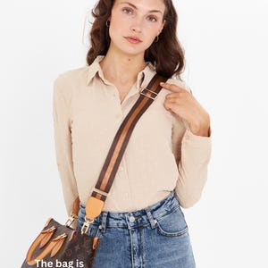 Op de afbeelding: Bruine handtas met een patroon en een gestreepte schouderriem. De tas heeft goudkleurige hardware en een lederen accent. De tekst "The bag is not for sale" is zichtbaar op de tas.
