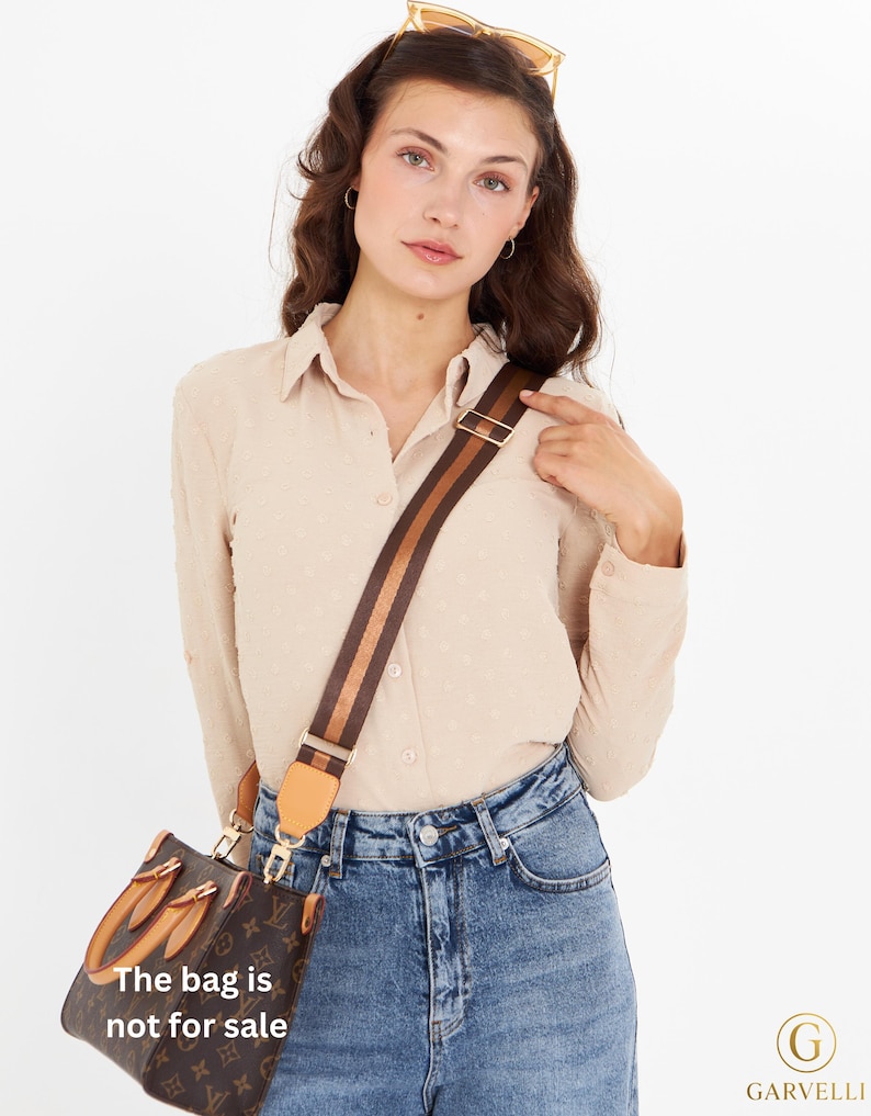 Op de afbeelding: Bruine handtas met een patroon en een gestreepte schouderriem. De tas heeft goudkleurige hardware en een lederen accent. De tekst "The bag is not for sale" is zichtbaar op de tas.