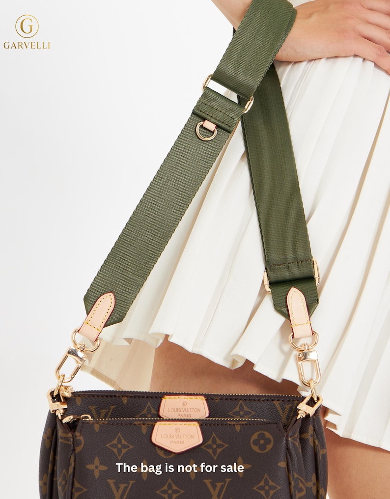May include: A brown handbag with a monogram pattern, featuring a green strap and gold-colored hardware. The bag has a zipper closure and two small tags. The text "The bag is not for sale" is visible.