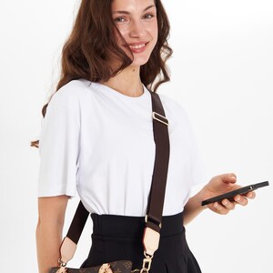 Op de afbeelding: Bruine monogram handtas met een donkerbruine schouderriem. De tas heeft goudkleurige hardware en een lichtgekleurde afwerking. De tekst "The bag is not for sale" is zichtbaar op de tas.