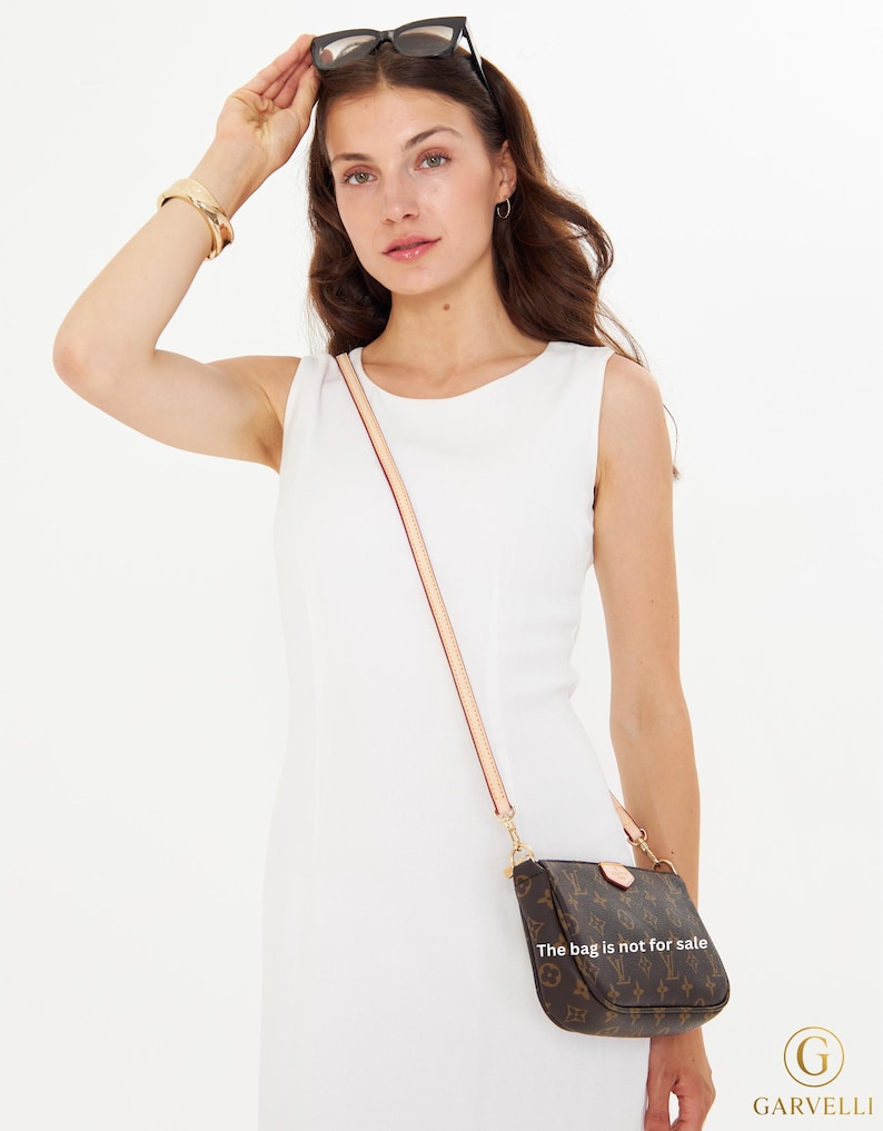 Puede incluir: Un bolso bandolera marr&oacute;n con un estampado de monograma y una correa clara. El bolso lo lleva una persona con un vestido blanco. El texto en el bolso dice "La bolsa no est&aacute; a la venta."