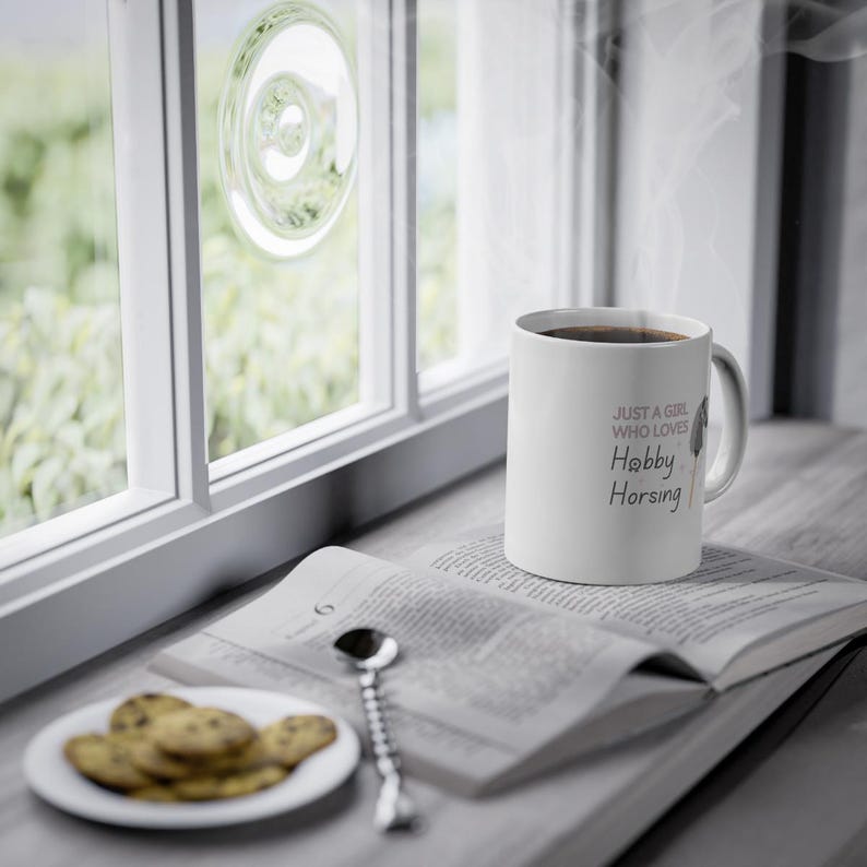 May include: White ceramic mug with a black handle. The mug has the text "Just a girl who loves Hobby Horsing" printed on it in pink and black.