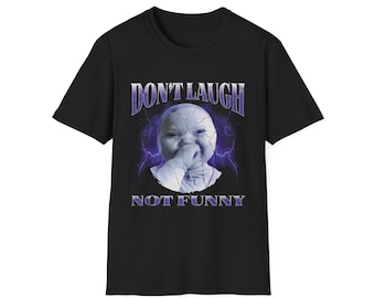 May include: Black t-shirt with a graphic featuring a baby's face with a cracked effect, surrounded by purple lightning. The text "DON'T LAUGH" is above the image, and "NOT FUNNY" is below.