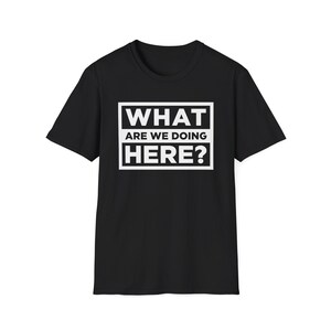 Puede incluir: Camiseta negra con el texto blanco "WHAT ARE WE DOING HERE?" dentro de un rectángulo blanco. La camiseta tiene mangas cortas y cuello redondo. El texto está en negrita, fuente sans-serif.