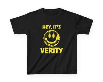 Może przedstawiać: Czarny t-shirt z krótkim rękawem z żółtą, postarzaną grafiką przedstawiającą uśmiechniętą buźkę. Nad buźką znajduje się napis "HEY, IT'S", a pod nią napis "VERITY" wykonany pogrubioną, żółtą czcionką o postarzanym wyglądzie.