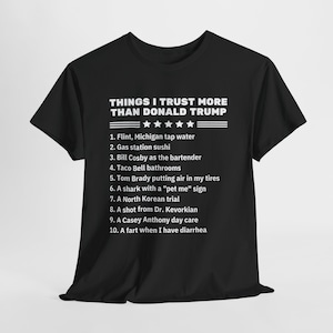 Könnte beinhalten: Schwarzes T-Shirt mit weißem Text, der "Things I trust more than Donald Trump" lautet, gefolgt von einer Liste von zehn Dingen. Die Liste enthält "Flint, Michigan tap water", "Gas station sushi", "Bill Cosby as the bartender", "Taco Bell bathrooms", "Tom Brady putting air in my tires", "A shark with a "pet me" sign", "A North Korean trial", "A shot from Dr. Kevorkian", "A Casey Anthony day care", and "A fart when I have diarrhea".