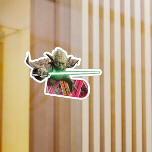 Puede incluir: Un personaje verde de Yoda de Star Wars montando un hoverboard rosa y amarillo con un sable de luz verde en la mano.