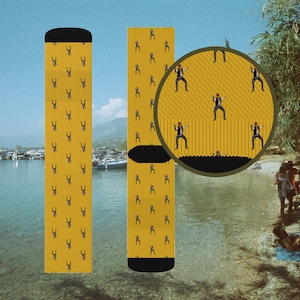 May include: Two pairs of yellow socks with a repeating pattern of a stick figure wearing a cowboy hat and holding a gun. The socks are on a white background.