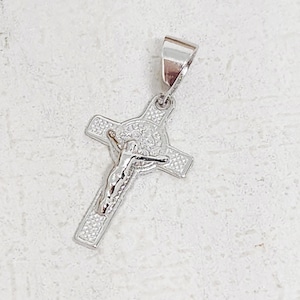 May include: A silver-colored pendant in the shape of a cross. The cross features a detailed depiction of Jesus Christ. The pendant has a loop at the top for a chain. The cross is decorated with small, textured details.