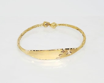 May include: A gold bangle bracelet with a decorative design and a flat, engraved plate.