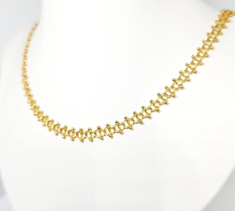 Pu&ograve; includere: Una collana a catena d'oro con un design delicato e intricato. La catena &egrave; composta da piccoli anelli rotondi che sono collegati in un motivo ripetitivo.