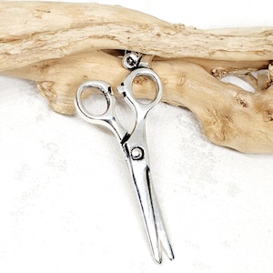 May include: A silver-toned pair of scissors charm pendant. The charm is hanging from a piece of driftwood.