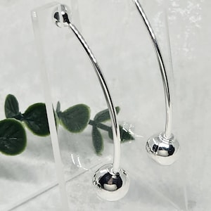 May include: A pair of silver hoop earrings with a curved design and a round ball at each end.