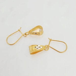 May include: A pair of gold-coloured earrings. Each earring features a textured, teardrop-shaped body and a simple hook. The design includes a small, decorative element in the centre of each earring.