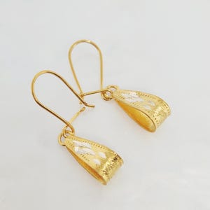 Puede incluir: Un par de pendientes dorados con diseño de gancho. Los pendientes tienen una sección inferior curvada y texturizada con un patrón de diamantes. Los ganchos son simples y curvados, diseñados para orejas perforadas.
