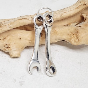 May include: Two silver wrench charms, one with a closed end and one with an open end, hanging from a silver ring.