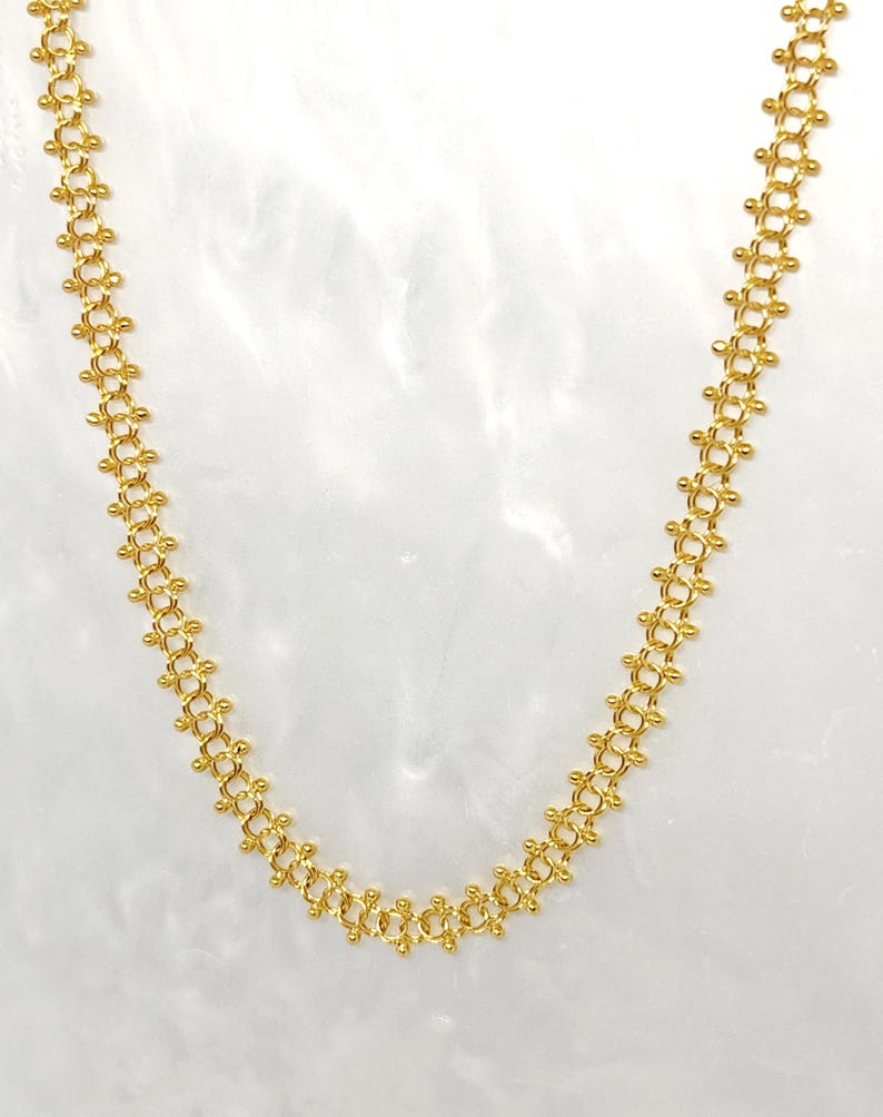 Pu&ograve; includere: Una collana a catena d'oro con un design delicato e intricato. La catena &egrave; composta da piccoli anelli rotondi che sono collegati in un motivo ripetitivo.
