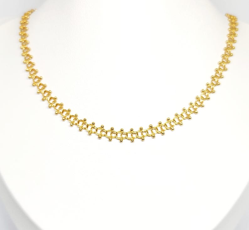 Pu&ograve; includere: Una collana a catena d'oro con un design delicato e intricato. La catena &egrave; composta da piccoli anelli rotondi che sono collegati tra loro in un motivo ripetitivo.