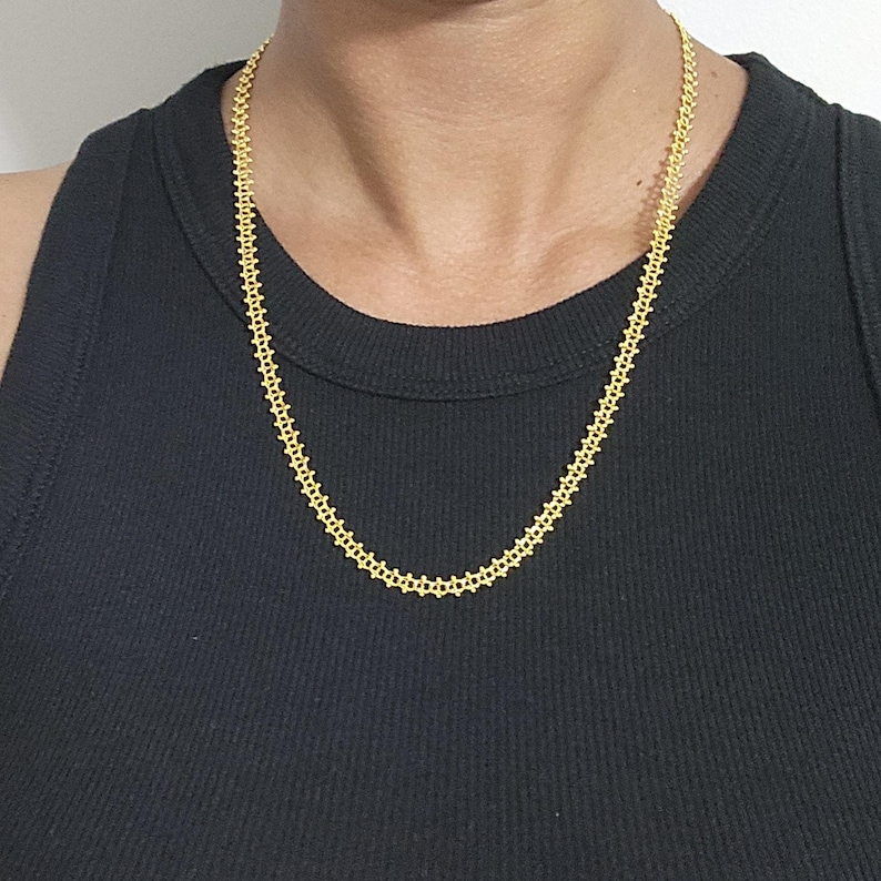 Pu&ograve; includere: Una collana a catena d'oro con un design delicato e intricato. La catena &egrave; composta da piccoli quadrati collegati.